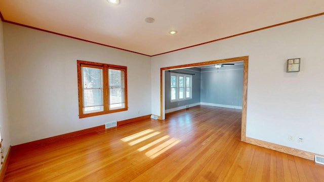 empty room with light wood-type flooring, baseboards, visible vents, and crown molding