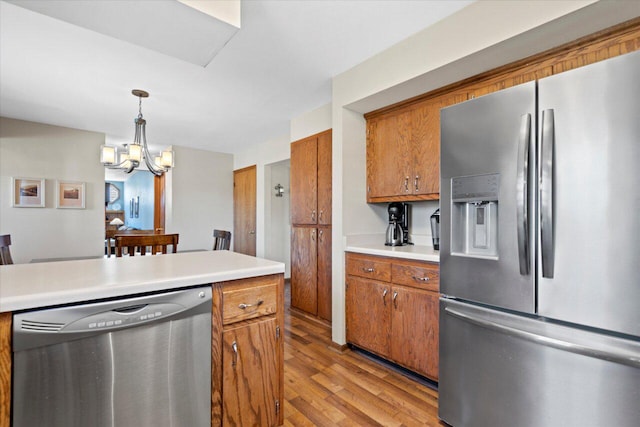 kitchen with a notable chandelier, stainless steel appliances, brown cabinetry, light wood finished floors, and light countertops