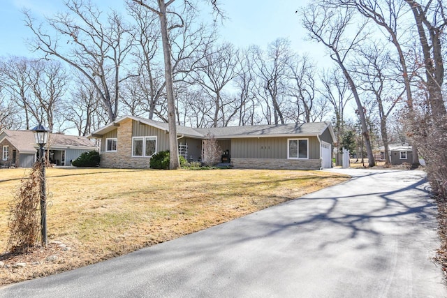 view of front of property with stone siding, board and batten siding, a front yard, and a garage