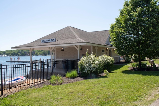 view of property exterior with a lawn, a shingled roof, a water view, and fence