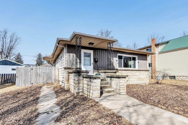 view of front of house with fence, board and batten siding, and stone siding