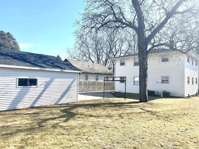 rear view of property with central air condition unit, a lawn, and fence