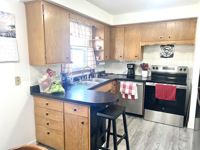 kitchen with a sink, open shelves, dark countertops, appliances with stainless steel finishes, and light wood finished floors