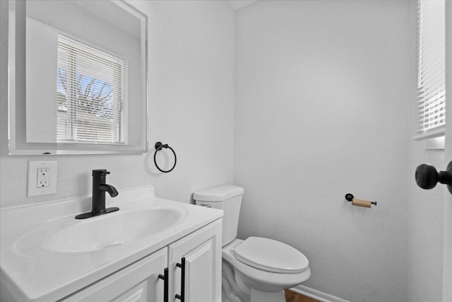 half bathroom with vanity, toilet, and baseboards