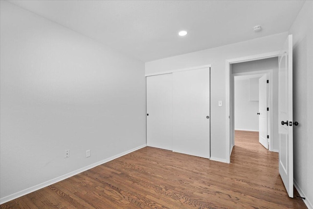 unfurnished bedroom featuring recessed lighting, wood finished floors, baseboards, and a closet