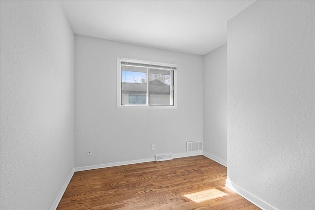 empty room featuring wood finished floors, visible vents, a textured wall, and baseboards