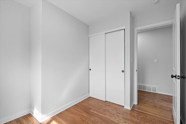 unfurnished bedroom with wood finished floors, visible vents, a closet, and baseboards