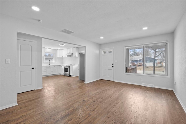 unfurnished living room featuring visible vents, baseboards, and wood finished floors