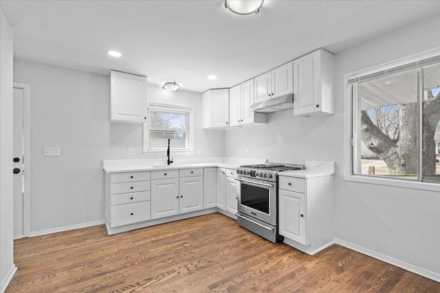 kitchen featuring a sink, dark wood-type flooring, white cabinets, under cabinet range hood, and gas range