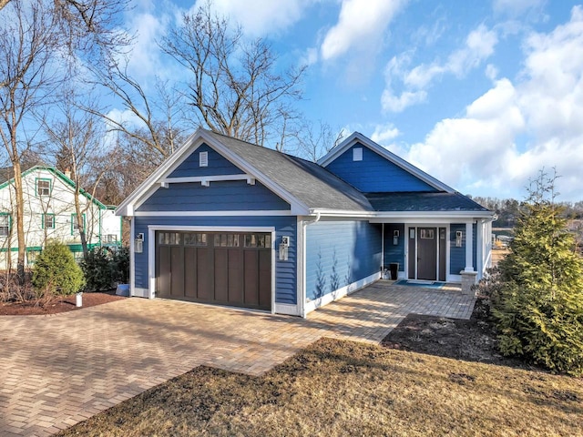 view of front of property with decorative driveway, an attached garage, and a shingled roof