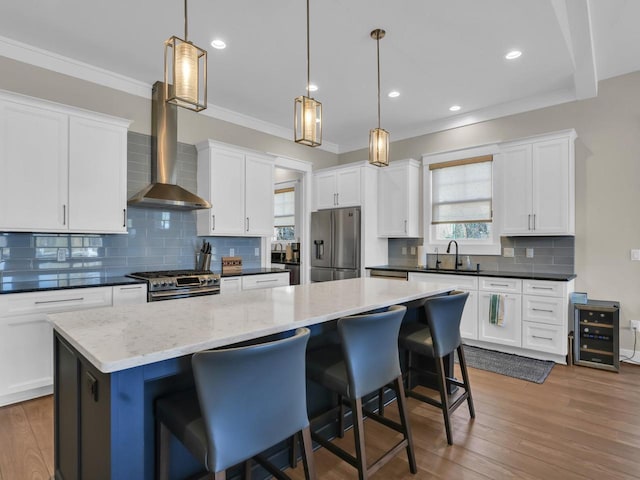 kitchen featuring a sink, a kitchen island, wood finished floors, appliances with stainless steel finishes, and wall chimney exhaust hood