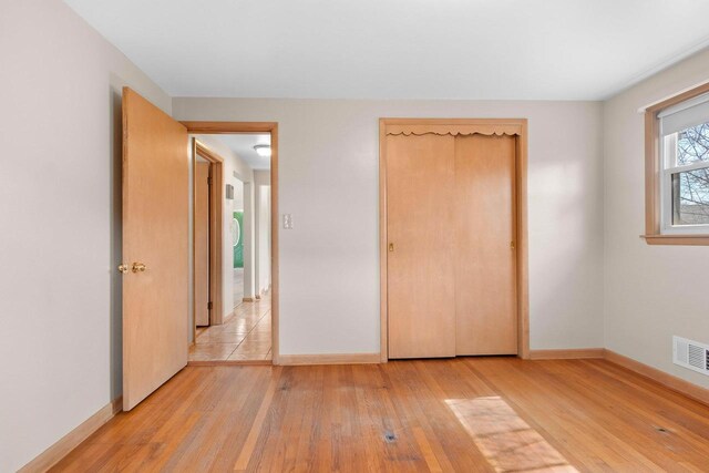 unfurnished bedroom featuring visible vents, baseboards, light wood-style floors, and a closet