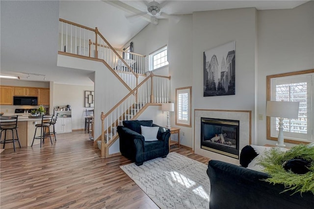 living area featuring ceiling fan, stairway, light wood-style floors, a glass covered fireplace, and high vaulted ceiling