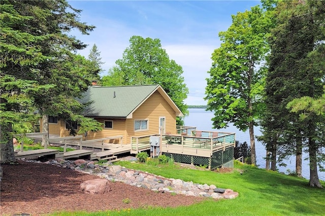 back of property with a lawn and a deck with water view