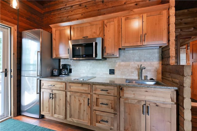 kitchen with wooden walls, light stone counters, a sink, appliances with stainless steel finishes, and tasteful backsplash