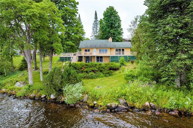 back of property with a chimney, a yard, and a water view