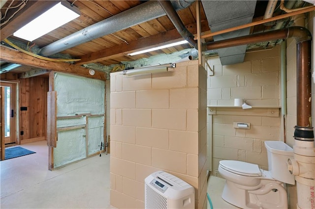 bathroom with toilet, concrete floors, and concrete block wall