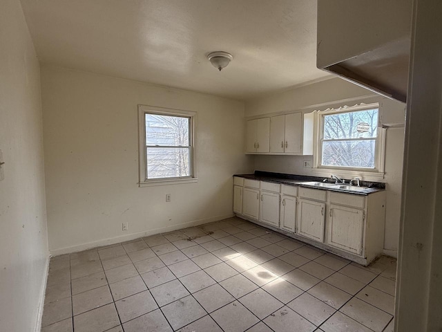 kitchen with a sink, dark countertops, white cabinetry, light tile patterned floors, and baseboards