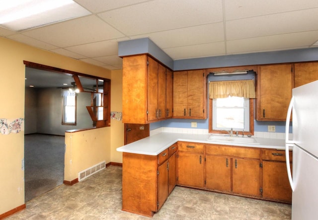 kitchen featuring brown cabinetry, visible vents, freestanding refrigerator, and a sink