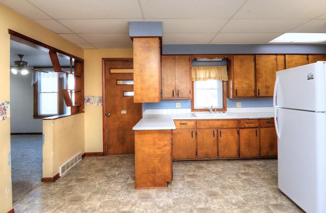 kitchen with visible vents, freestanding refrigerator, a sink, light countertops, and brown cabinets