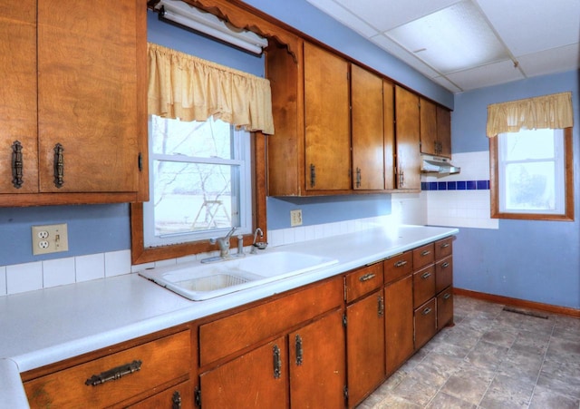 kitchen featuring a drop ceiling, brown cabinets, light countertops, and a sink