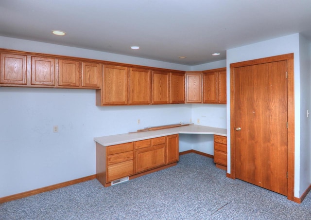 kitchen featuring baseboards, brown cabinetry, and built in study area