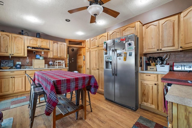 kitchen featuring light wood finished floors, a ceiling fan, backsplash, stainless steel fridge, and light countertops