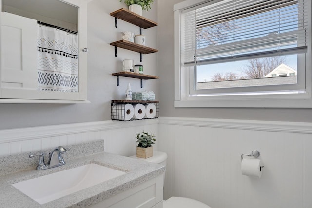 full bathroom featuring vanity, toilet, a shower with curtain, and a wainscoted wall