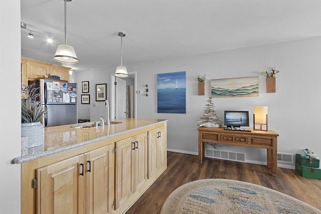 kitchen with a sink, light brown cabinets, light stone counters, freestanding refrigerator, and dark wood-style flooring