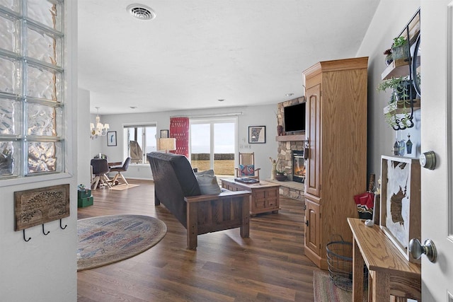 living area with visible vents, dark wood-type flooring, a fireplace, and a notable chandelier