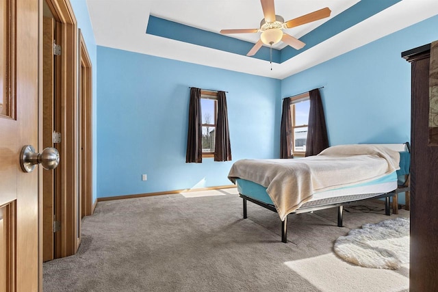 carpeted bedroom with a tray ceiling, baseboards, and ceiling fan