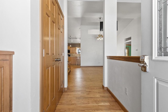 hall featuring baseboards, lofted ceiling, and light wood-style floors