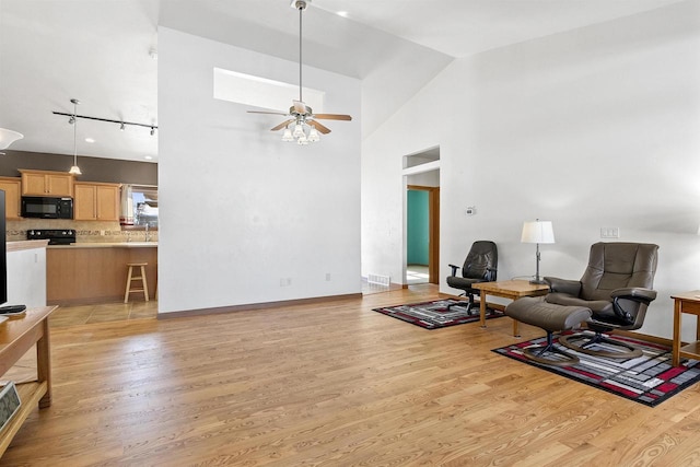 sitting room with light wood finished floors, visible vents, baseboards, high vaulted ceiling, and a ceiling fan