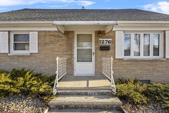 entrance to property with brick siding and a shingled roof