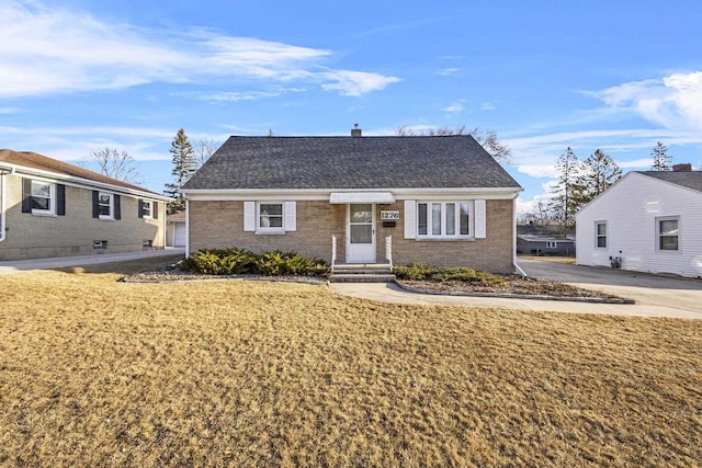 view of front of property with brick siding, a front yard, and roof with shingles