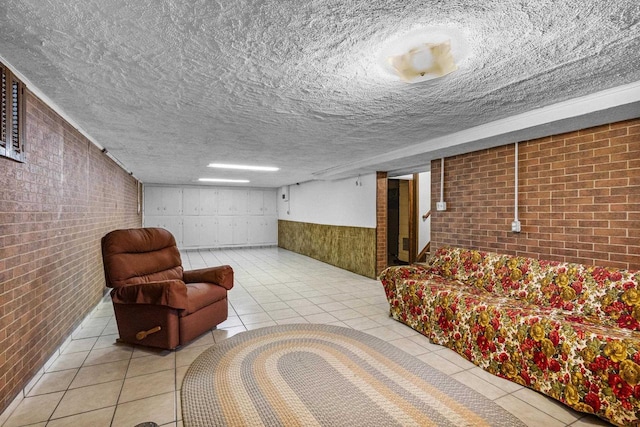 living area featuring tile patterned floors, wainscoting, brick wall, and a textured ceiling