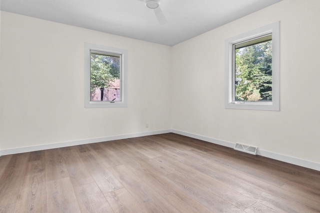 spare room featuring visible vents, plenty of natural light, wood finished floors, and a ceiling fan