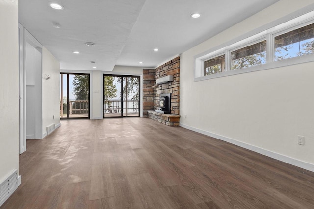 unfurnished living room with visible vents, baseboards, a stone fireplace, and wood finished floors