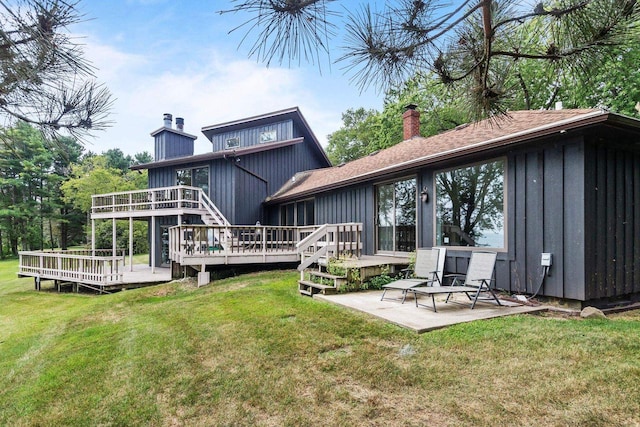 rear view of house with a patio, a wooden deck, a chimney, a lawn, and board and batten siding