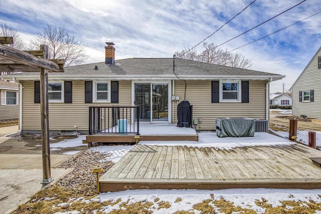 snow covered back of property with a wooden deck and a chimney