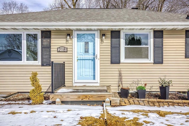 snow covered property entrance featuring a shingled roof