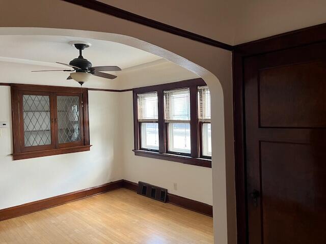 empty room with light wood finished floors, visible vents, baseboards, arched walkways, and a ceiling fan