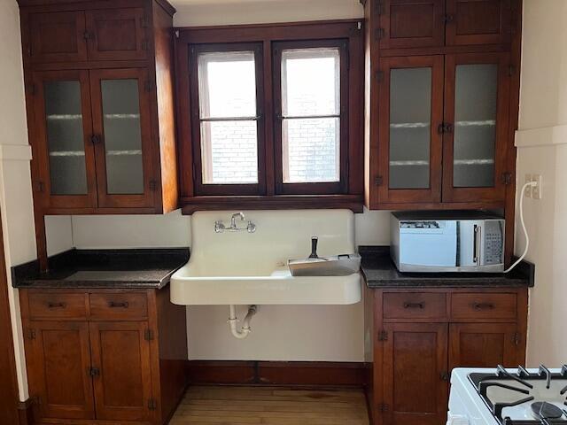 kitchen featuring dark countertops, brown cabinets, glass insert cabinets, and a sink