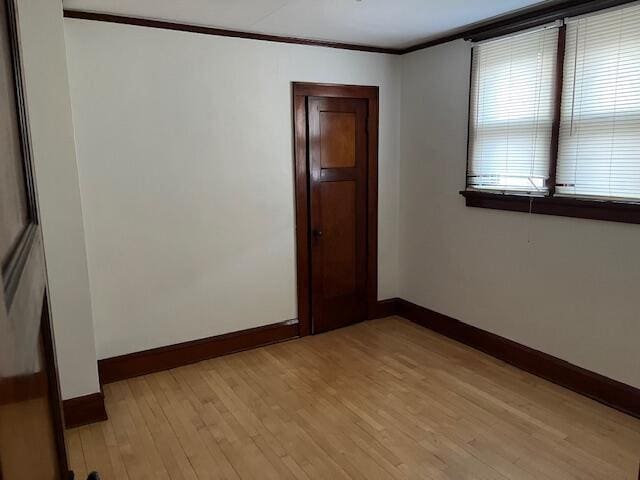 unfurnished room featuring crown molding, light wood-style floors, and baseboards