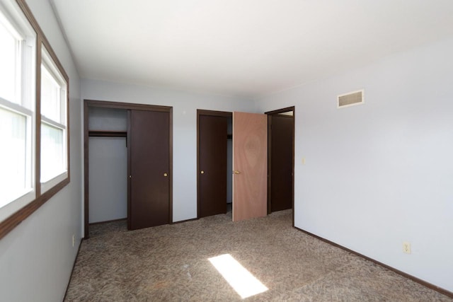 unfurnished bedroom with visible vents, multiple closets, and carpet flooring