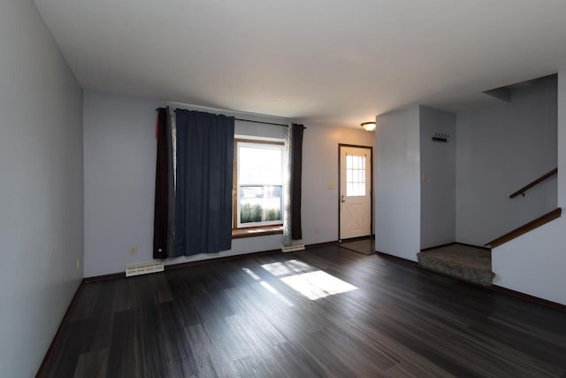 unfurnished living room featuring dark wood-type flooring, baseboards, and visible vents