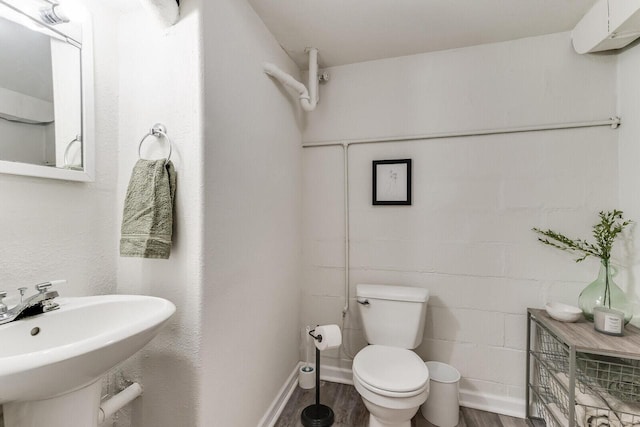 bathroom with toilet, a sink, wood finished floors, concrete block wall, and baseboards