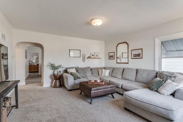 living area featuring baseboards, visible vents, arched walkways, and light carpet