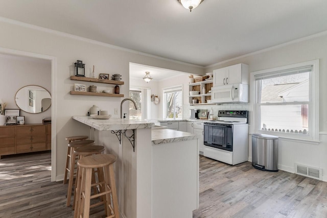 kitchen with white appliances, visible vents, a breakfast bar, open shelves, and a peninsula