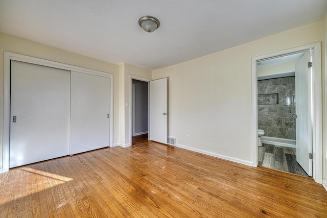 unfurnished bedroom featuring visible vents, baseboards, a closet, wood-type flooring, and connected bathroom